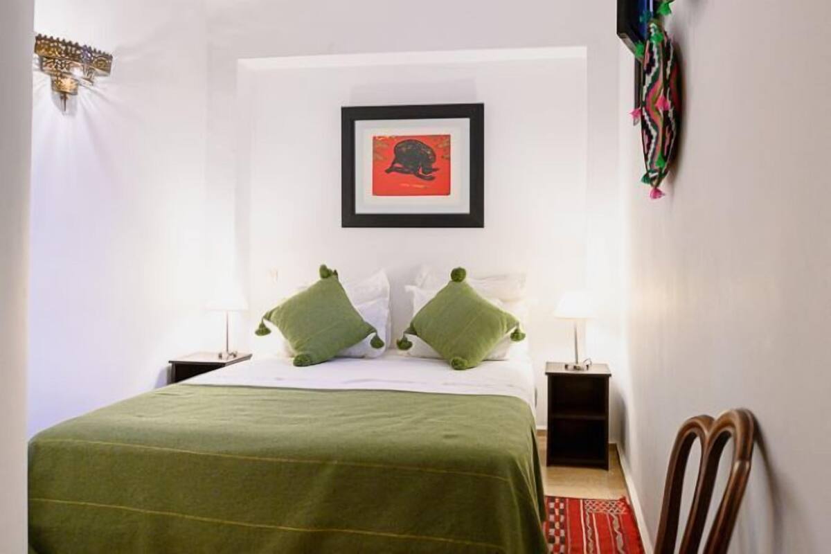 Habitación de hotel ordenada con una cama, dos mesitas de noche, un cuadro en la pared y una silla.