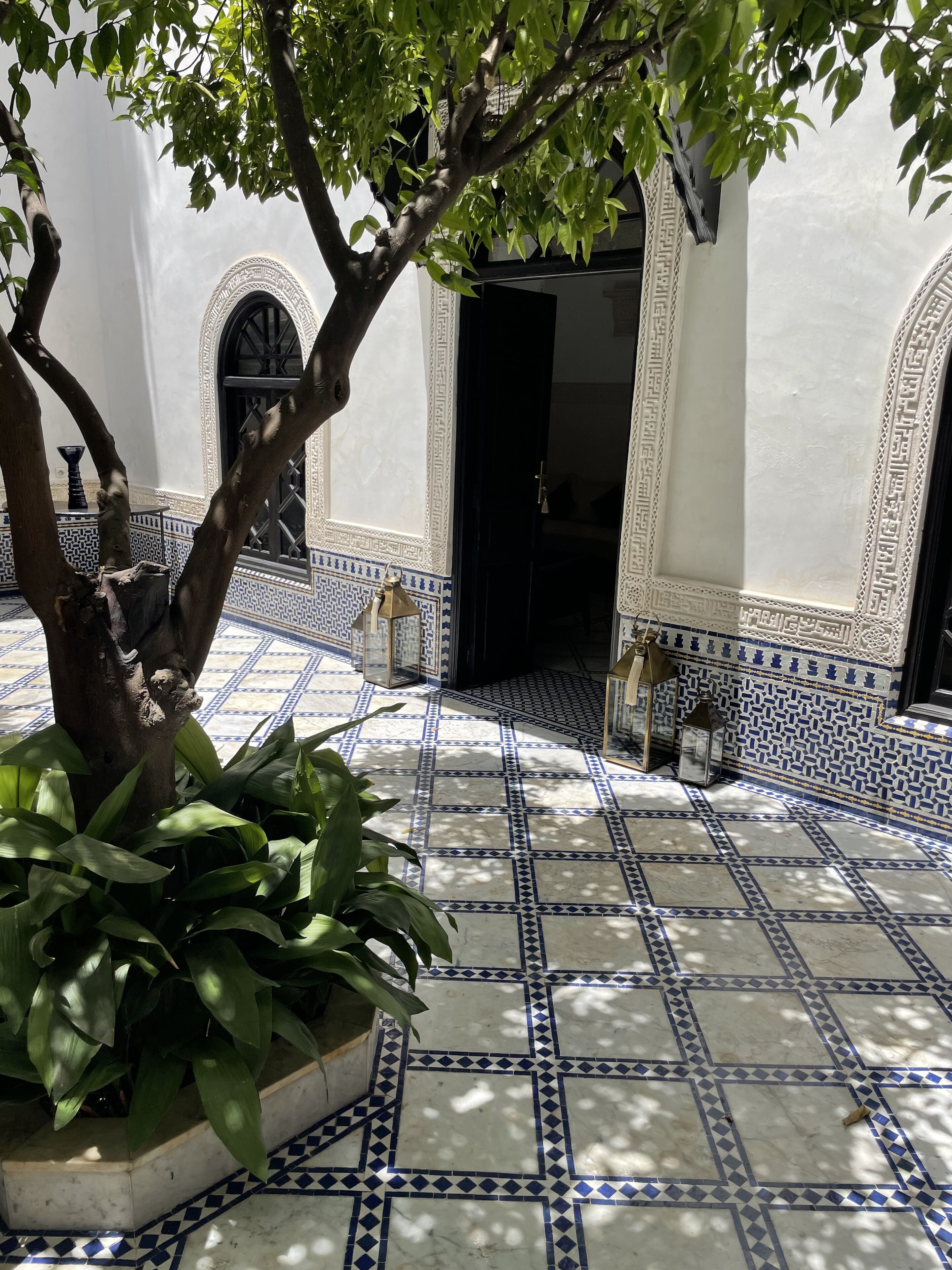 Um pátio com chão de azulejos, uma árvore e uma porta com arcos decorativos.