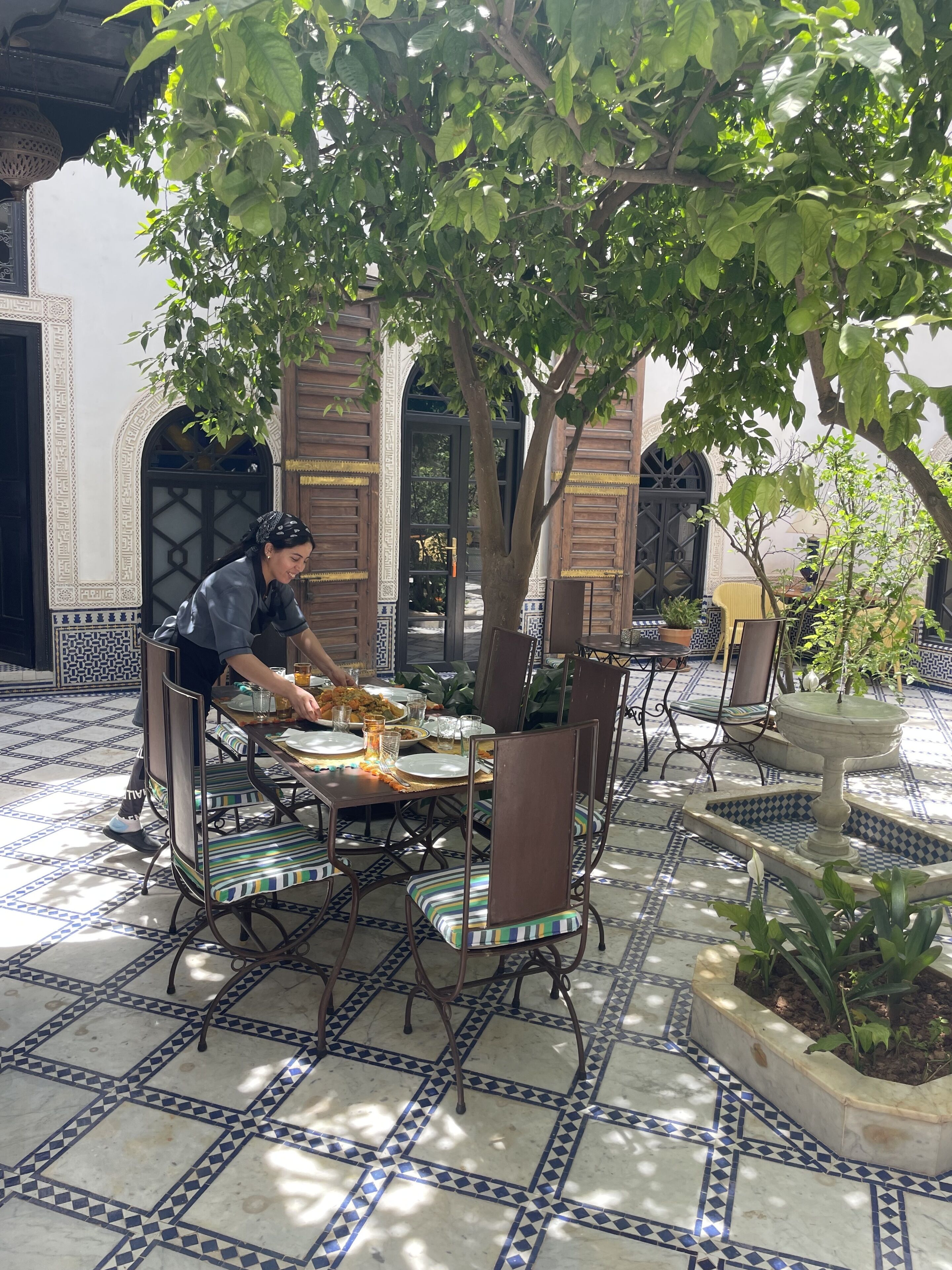Un comedor con suelo de baldosas, una mesa dispuesta para dos personas y un árbol que da sombra.