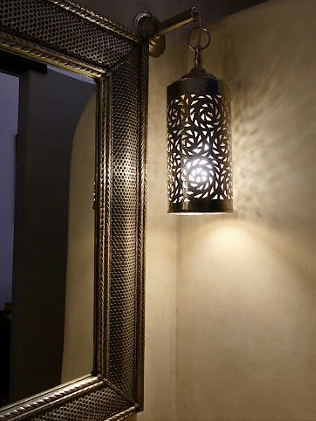 Un baño con un espejo grande y un farol colgante con intrincados diseños recortados.