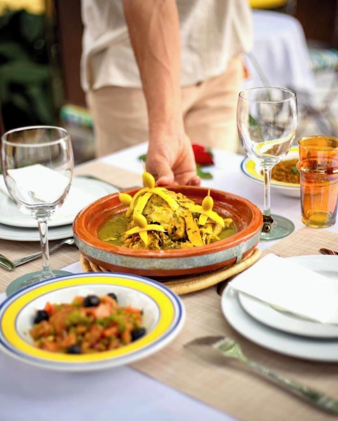 A dining table with a large pot of stew, a bowl of salad, and several glasses of water.