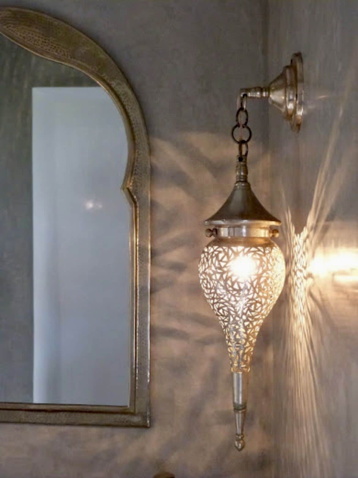 Un luminaire mural orné d’un motif géométrique, un miroir avec un cadre travaillé et un mur à texture.