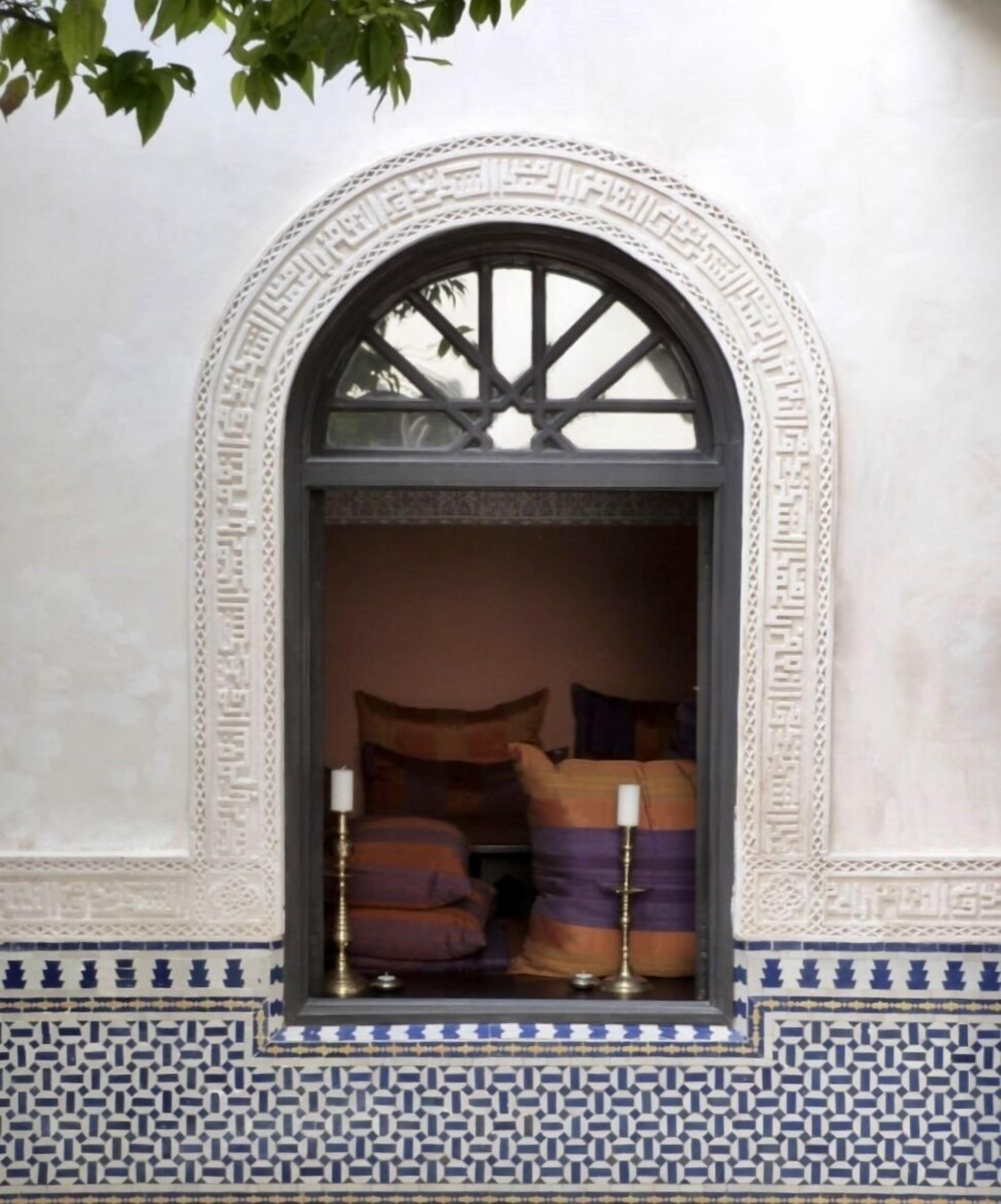 A room with a large arched window, patterned wall tiles, and a bed with pillows and candles.