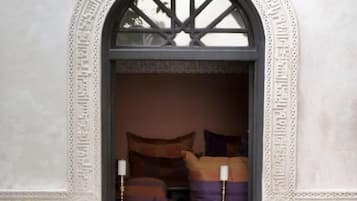 A room with a large arched window, patterned wall tiles, and a bed with pillows and candles.