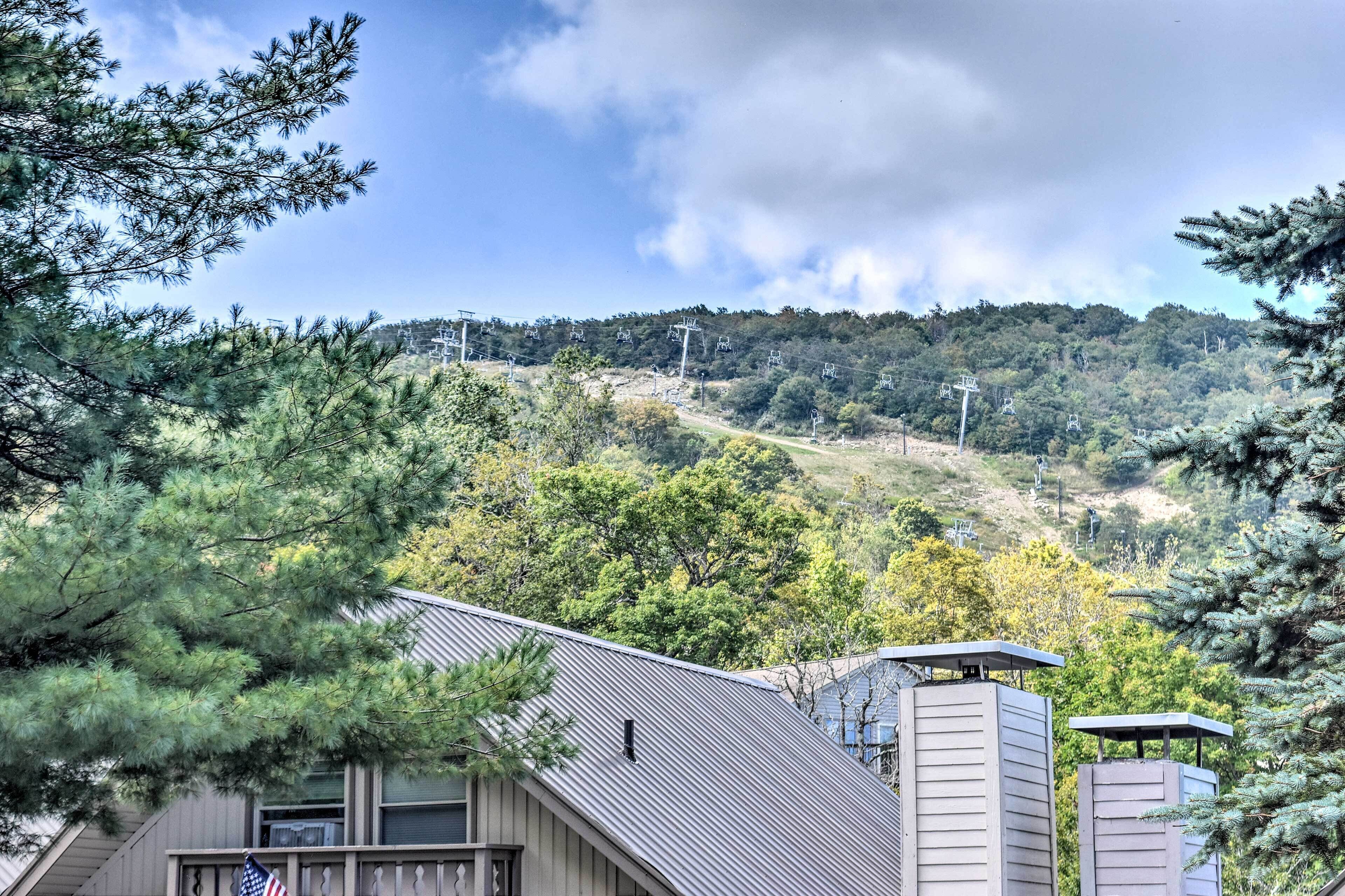 Un edificio residencial con techo metálico, rodeado de árboles y un paisaje montañoso al fondo.