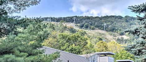 Un edificio residencial con techo metálico, rodeado de árboles y un paisaje montañoso al fondo.