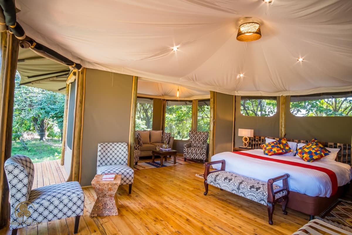 A tented accommodation with a large bed, two sofas, a small table, and a chair.
