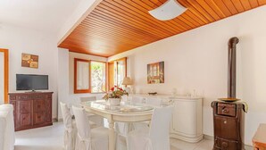 A dining area with a round table, white chairs, a wooden ceiling, and a stove. - semidetached beach villa in front of eolian island near Milazzo: Tindari (furnari)