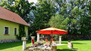 Eine Terrasse mit einem roten Sonnenschirm, Steinpfeilern und einem gelben Gebäude mit rotem Dach.