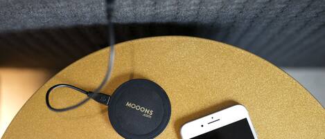 Un teléfono inteligente sobre una superficie dorada, con un cable de carga y un objeto circular negro que dice 'MOONS.com'.