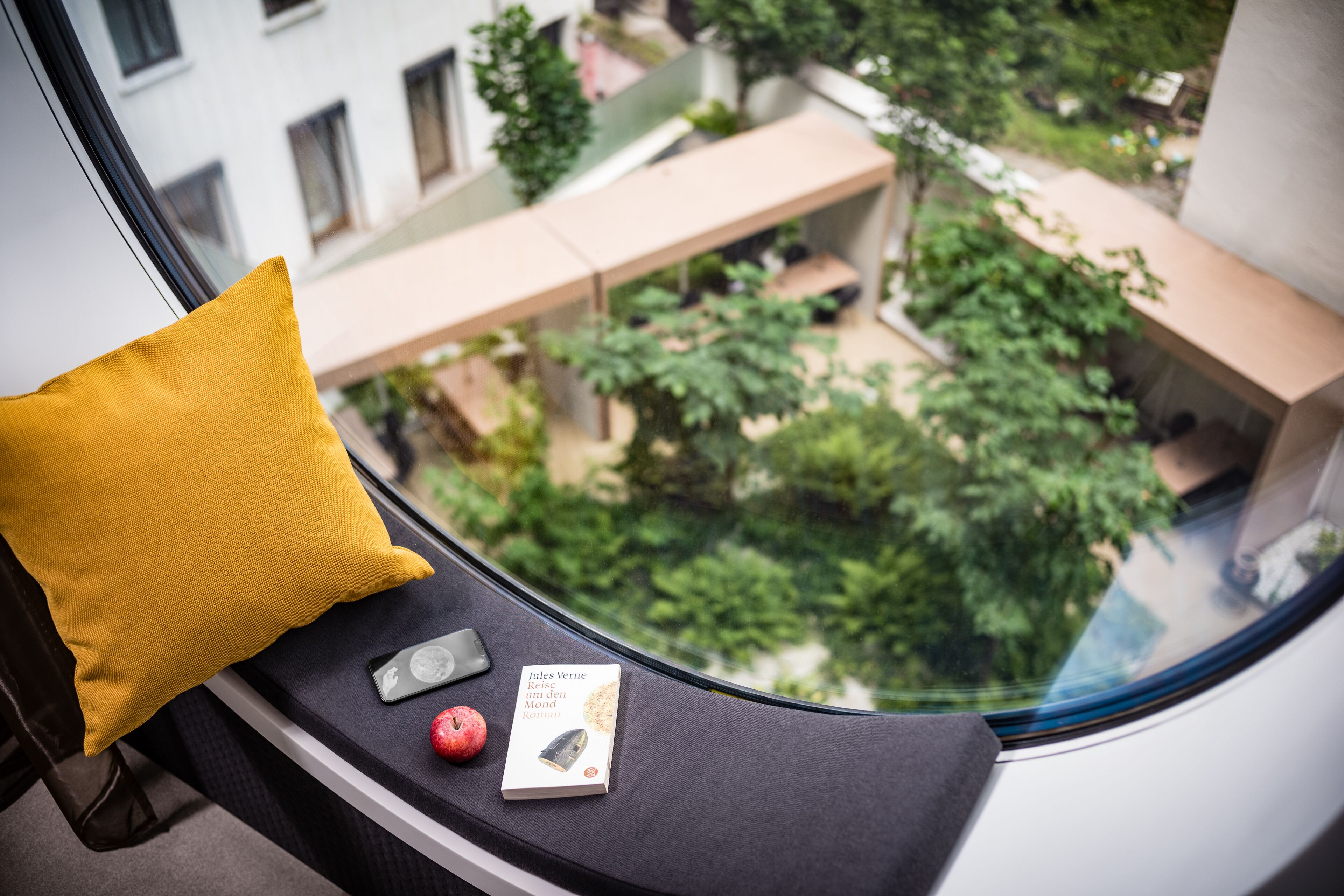 A window seat with a yellow pillow, a book, and a red apple.