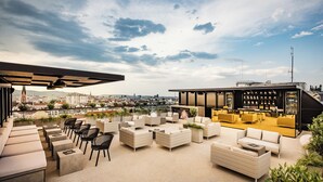 A rooftop bar with outdoor seating, a bar area with shelves of bottles, and a city view in the background. - MOOONS (Vienna)