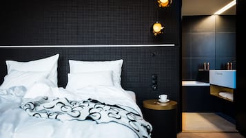 Een moderne hotelkamer met een groot bed, een nachtkastje met een kopje en een donkere, structuurrijke wand.