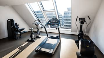 Un gimnasio moderno con cinta de correr, elíptica y máquina de pesas, ventanas amplias con vista a la ciudad.