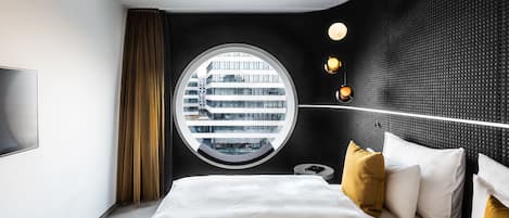 Una habitación de hotel moderna con una cama grande, un ventanal redondo y vistas a la ciudad.