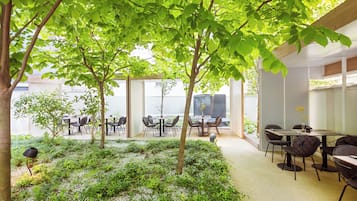 An outdoor seating area with tables and chairs, surrounded by greenery and trees.