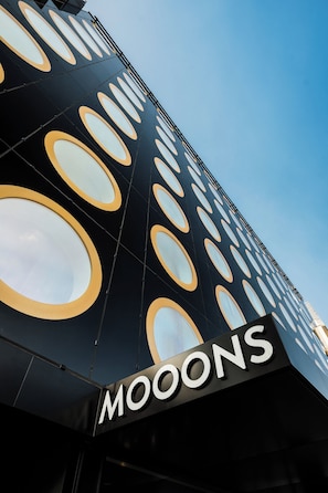A building facade with a repeating pattern of circular windows and the word "MOOONS" in large letters.