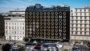 A modern building with a facade of circular patterns and the word "MONOS" visible. - MOOONS (Vienna)