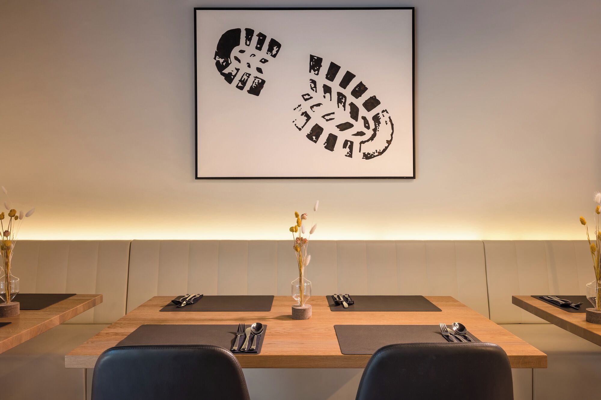 A dining area with a wooden table, black placemats, and a framed artwork above.