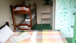 A bunk bed room with a checkered bedspread, a small table with a patterned tablecloth, and a fan on the wall. - Pousada Recanto Verde (Sao Benedito do Sul)