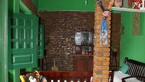 A room with a brick wall, a wooden bench, a green door, and a television on a wooden stand. - Pousada Recanto Verde (Sao Benedito do Sul)