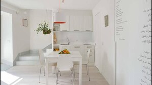 A modern kitchen with white cabinets, a white countertop, and a hanging plant. - Community Rooms & Wine (Favara)