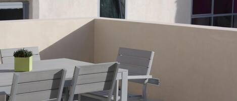 A modern outdoor patio with a table and chairs, a potted plant, and a building in the background.