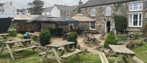 A courtyard with wooden picnic tables and umbrellas, stone buildings, and a stone wall.