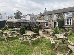 A courtyard with wooden picnic tables and umbrellas, stone buildings, and a stone wall.