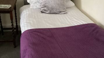 A bed with a purple blanket, white pillows, and a grey headboard in a room with a wooden nightstand.
