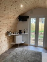 Una cocina compacta con paredes de madera, una encimera blanca, una cafetera y un televisor montado en la pared.