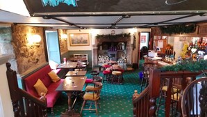 A cozy restaurant with a green carpet, wooden furniture, and a stone wall. - The Pirate Inn (Penzance)