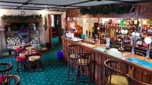 A bar area with wooden stools, a counter with a menu, and a variety of bottles and glasses. - The Pirate Inn (Penzance)