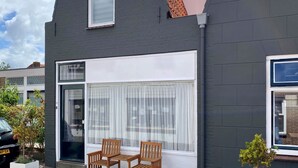 A modern house with a large garage door, a small patio with two wooden chairs, and a clear sky.