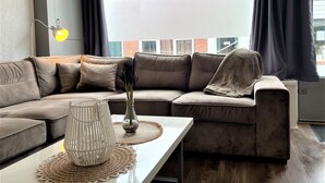 A modern living room with a sectional sofa, a glass coffee table, and a view of a red-roofed building outside.