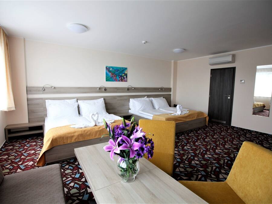 A hotel room with a bed, a sofa, a table with a vase of flowers, and a patterned floor.