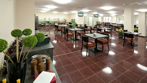 A spacious dining area with multiple tables and chairs, a counter with a cash register, and a large window providing natural light. - Hotel Arena (Chomutov)