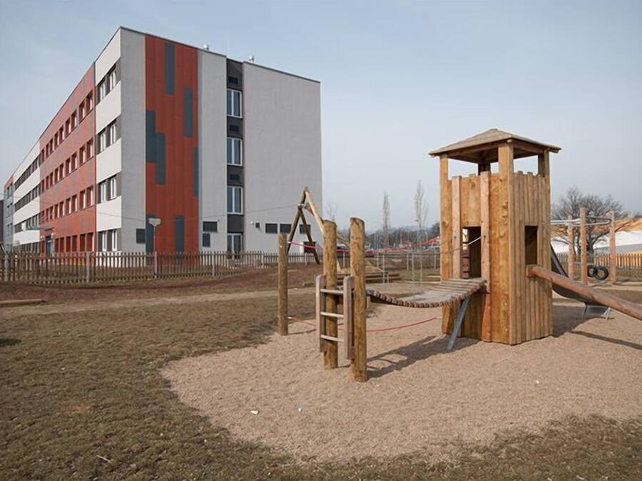 A playground with a wooden climbing structure and a slide, adjacent to a multi-story building with a modern design.