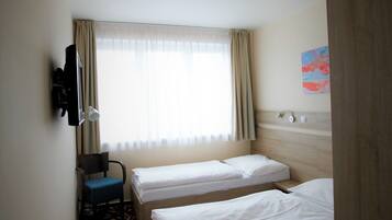 A hotel room with two single beds, a television, a desk, and a patterned floor.