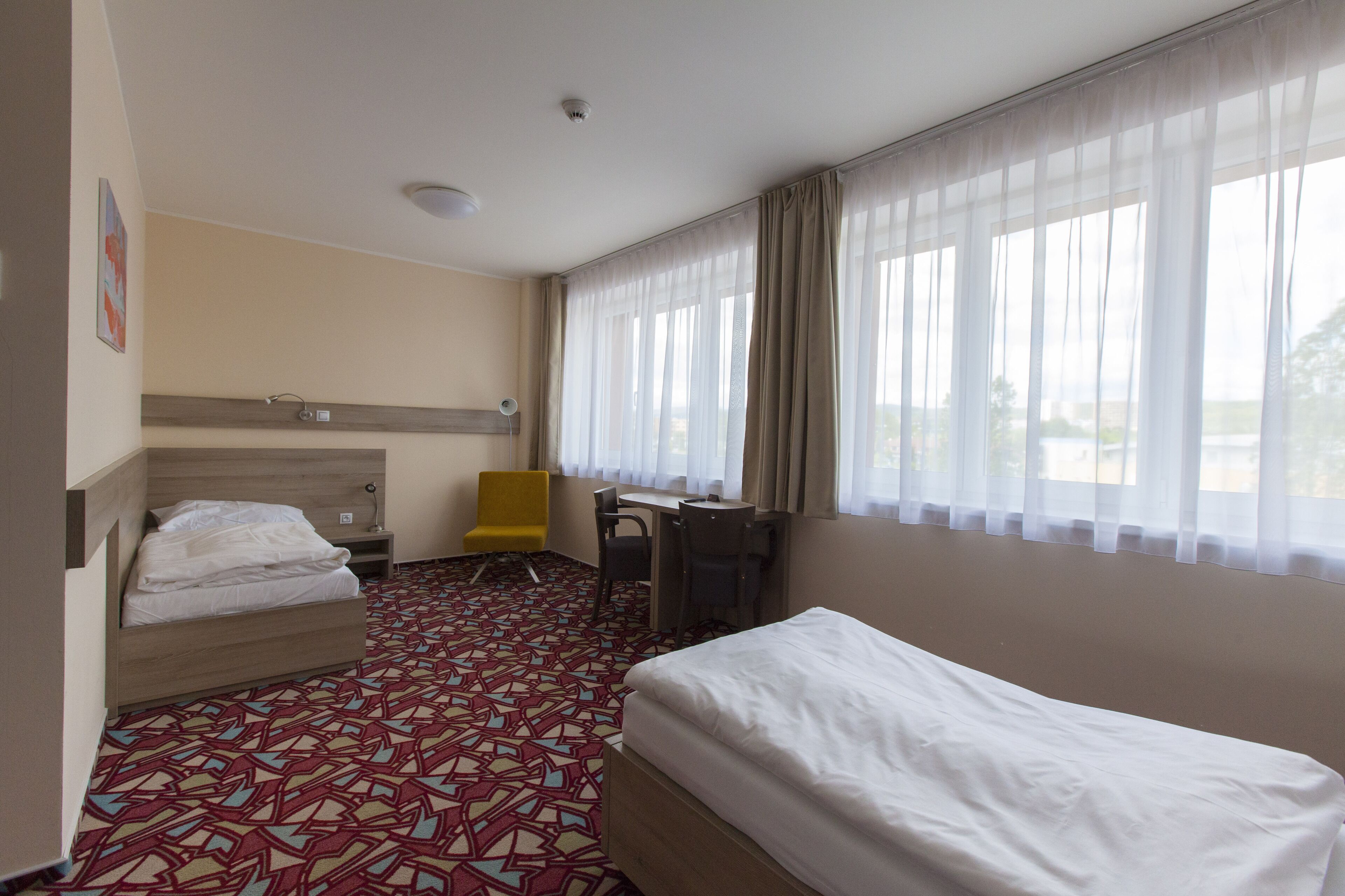 Habitación de hotel con cama, escritorio, silla y ventana con cortinas.