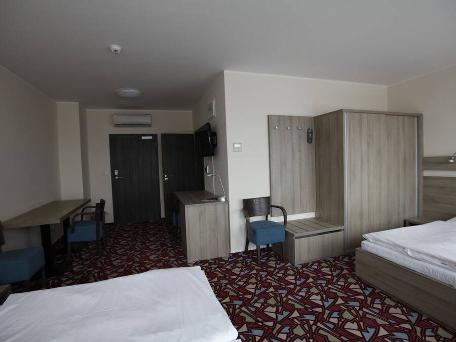 Hotellihuone, jossa on kaksi sänkyä, työpöytä, tuoli, vaatekaappi ja ilmastointilaite.