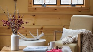 A cozy room with a wooden bench, a table with a vase, books, and a window with blinds. - Outpost: Alpine Cottage Four (Jackson)