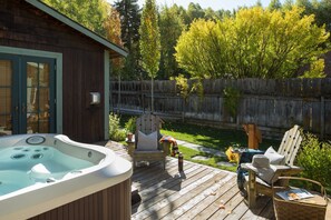 A wooden deck with a hot tub, two Adirondack chairs, and a small table with a basket and a book. - Outpost: Alpine Cottage Four (Jackson)