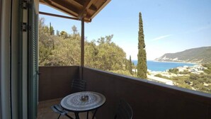 A balcony with a table and chairs, overlooking a coastal landscape with trees and a clear sky. - Lefkas Petra (Lefkada)