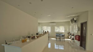 A spacious kitchen with a long counter, a dining area with a table and chairs, and a door on the right. - Lefkas Petra (Lefkada)