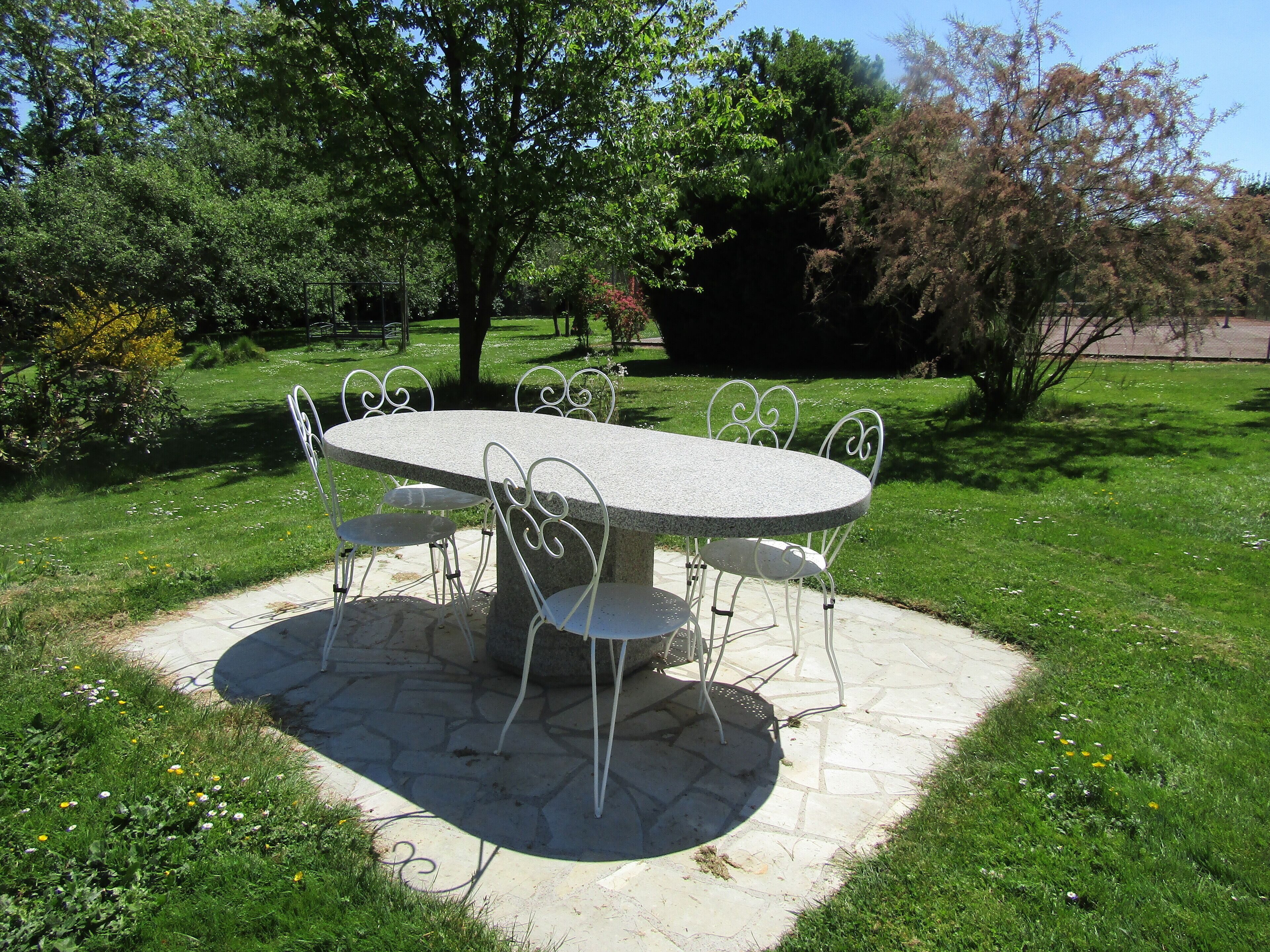 A stone table with metal chairs in a garden setting.