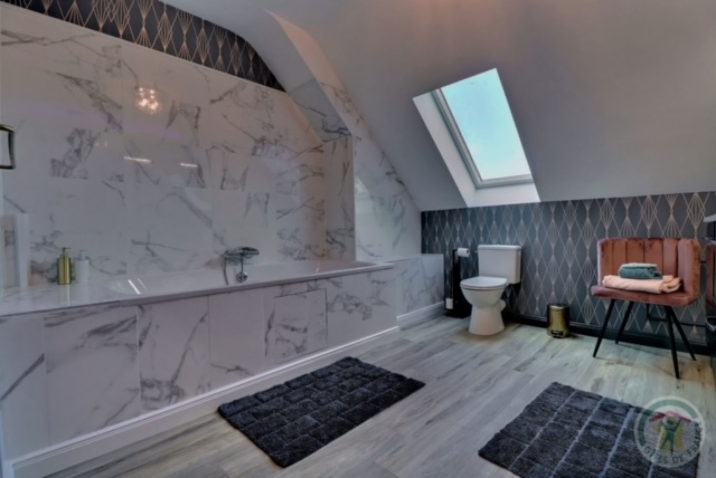 A modern bathroom with a marble vanity, a freestanding bathtub, a skylight, and a black rug on the floor.