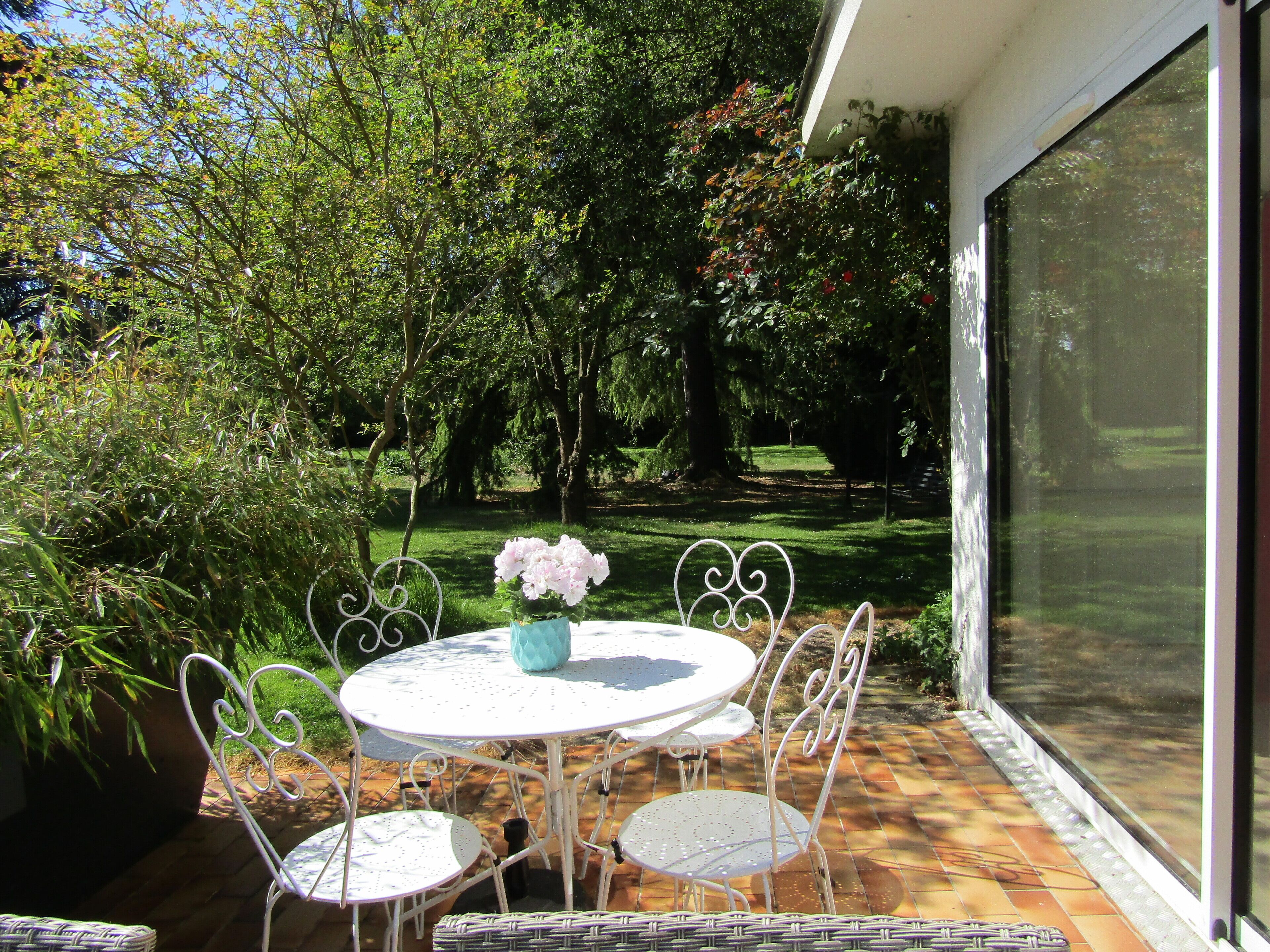 A patio with a round table and chairs, surrounded by lush greenery and trees.