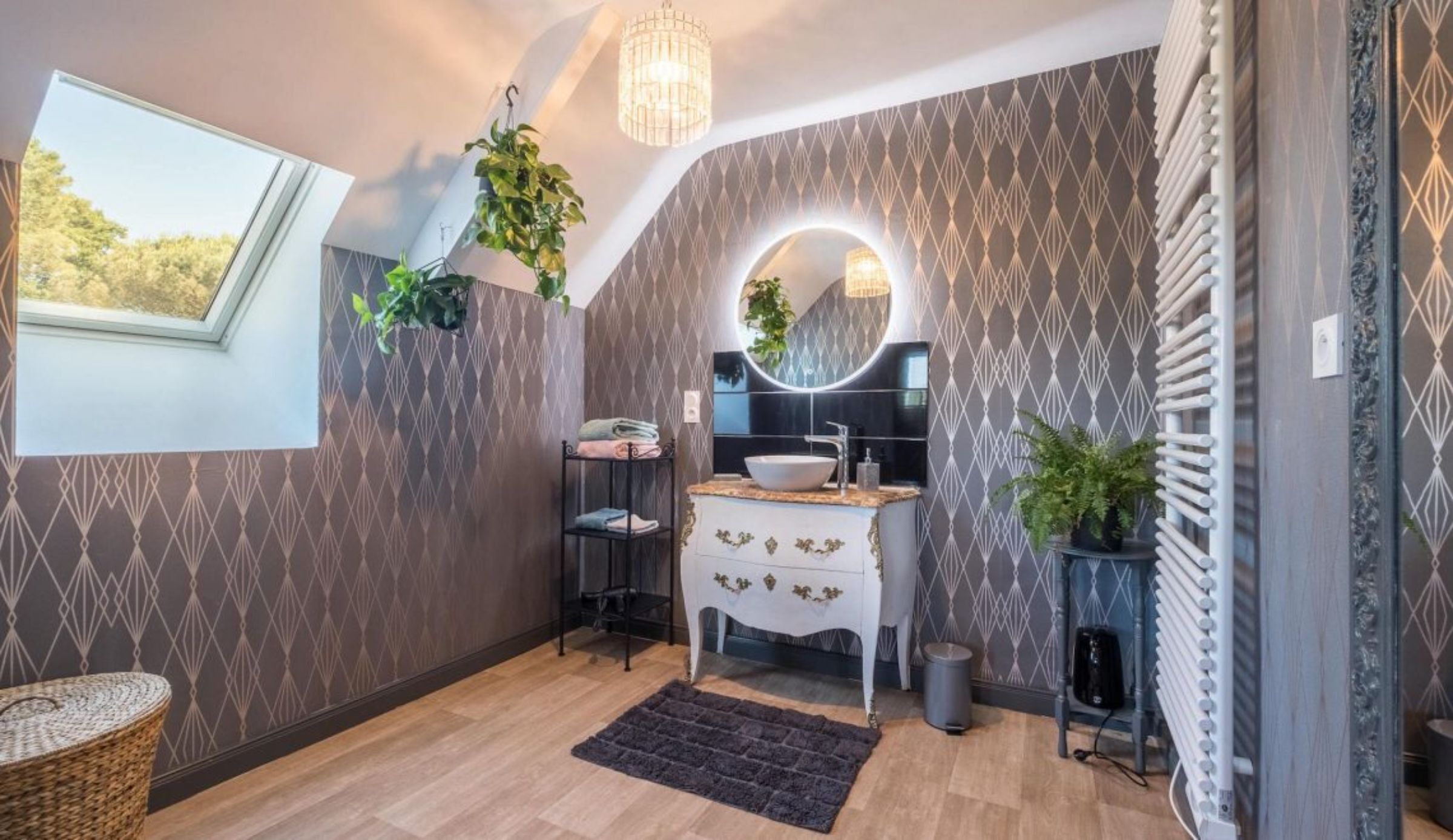 A modern bathroom with a skylight, a round mirror, a white vanity, and patterned wallpaper.