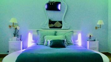 A circular bed with a white headboard and a flat mattress. There are two bedside tables with lamps and a small plant on each.